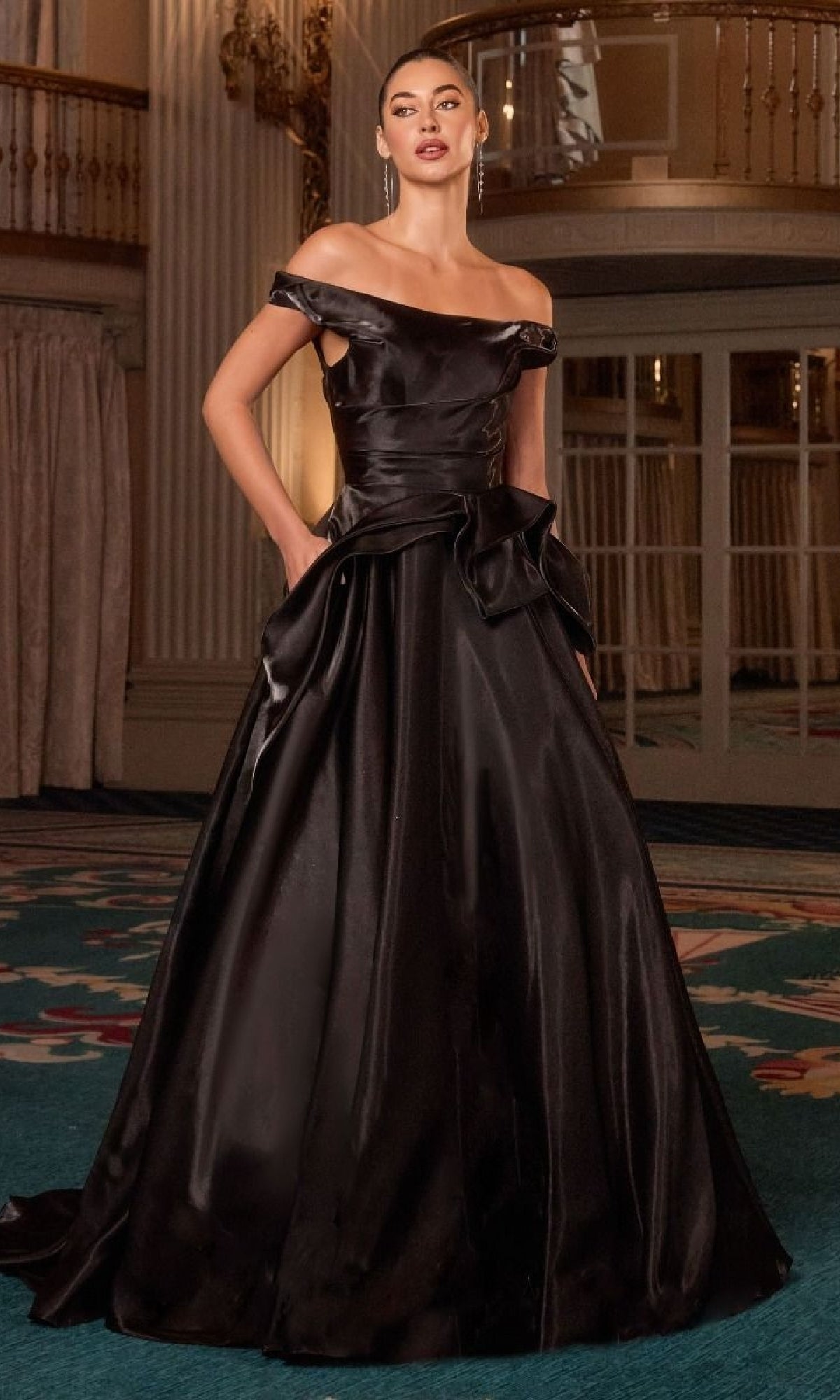 A woman stands indoors on a decorative carpet, wearing the Ladivine J885 Long Prom Dress—an off-the-shoulder satin gown with a full A-line skirt that exudes elegance and timeless sophistication.